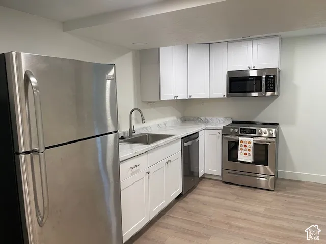 Kitchen featuring white cabinetry, stainless steel appliances, a stainless steel sink with a gooseneck faucet, light-toned countertops, and wood-finish flooring