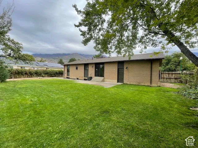 Expansive green lawn with mountain scenery, brick exterior, and a concrete patio