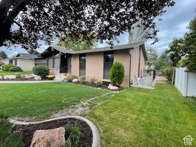 Brick exterior with a peaked roofline, front lawn, mature landscaping, and an adjacent fenced area