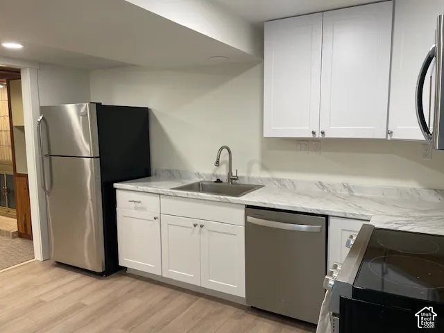 White shaker cabinetry with modern hardware, stainless steel appliances, stainless steel sink with a gooseneck faucet, light-toned wood-finish flooring, and light-toned countertops