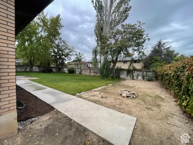 Expansive backyard featuring a partial manicured lawn, established perimeter fencing, mature trees, and a concrete pathway