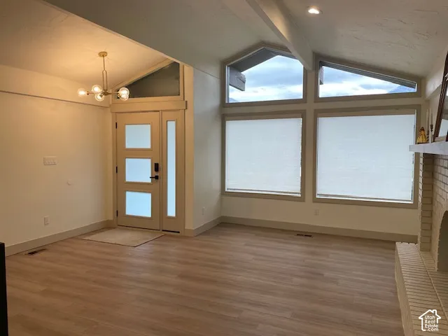 Wood-finish flooring, contemporary front door with frosted glass panels, modern chandelier, recessed lighting, and a brick fireplace