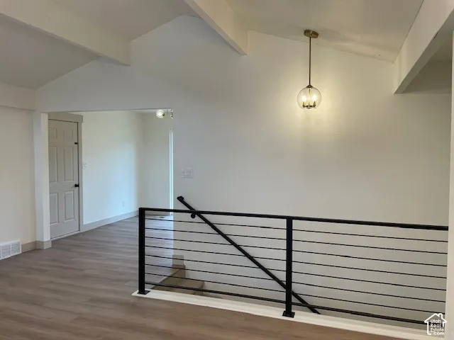 Vaulted ceiling with exposed beams, wood-finish flooring, contemporary pendant light fixture, and black metal railing