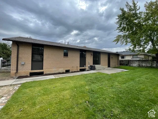 Brick exterior, asphalt shingle roof, concrete patio, mature trees, and a spacious lawn