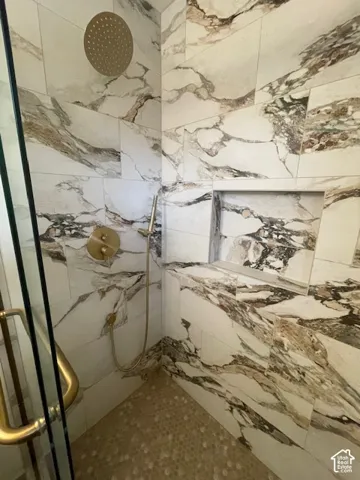 Walk-in shower with full-height patterned tile, built-in shelving, a built-in bench, a rainfall showerhead, and a handheld shower fixture
