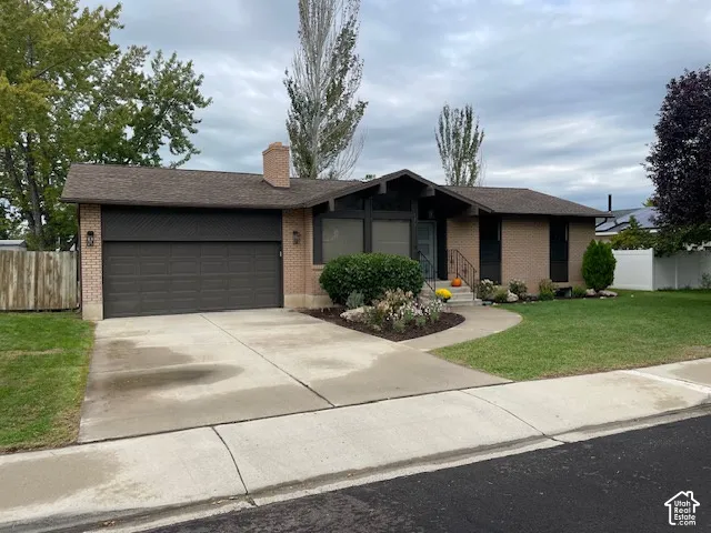 Brick exterior featuring a two-car garage, mature landscaping, and a concrete driveway