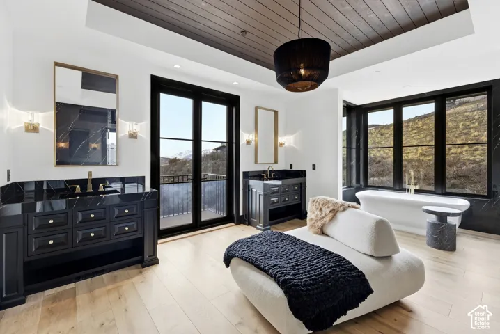 Wood-finish flooring, dark wood ceiling, freestanding tub, dark vanity with integrated sink, and black-framed windows