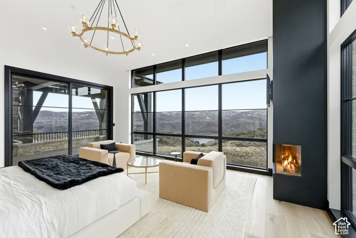Expansive floor-to-ceiling windows, built-in fireplace, light wood-finish flooring, and a gold-finish chandelier