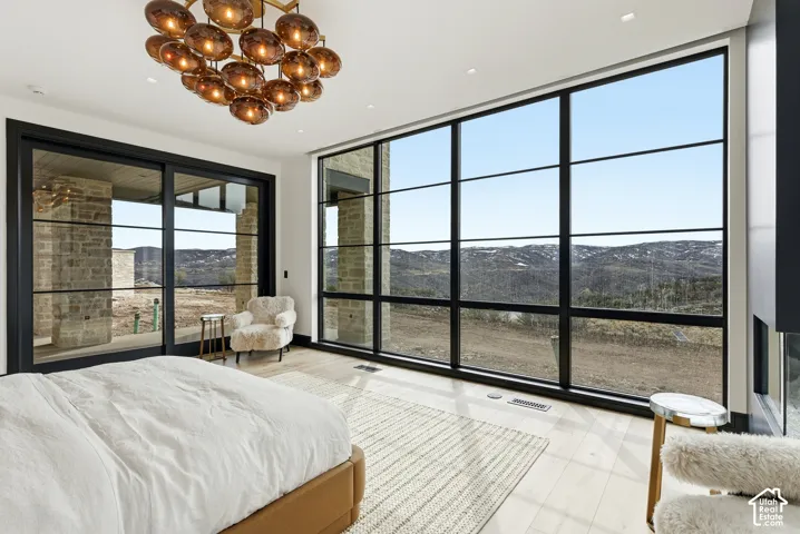 Expansive floor-to-ceiling windows, wood-finish flooring, a contemporary ceiling light fixture, and a built-in linear fireplace