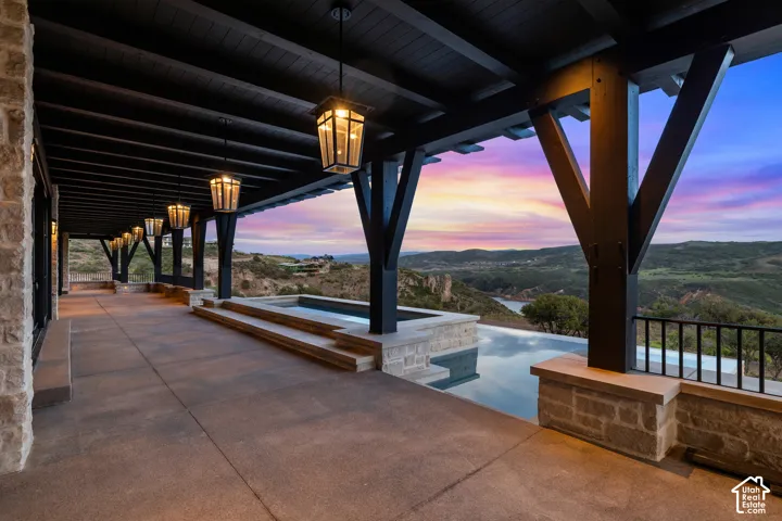 Expansive covered patio featuring a dark wood pergola, stone-clad walls, and a built-in spa