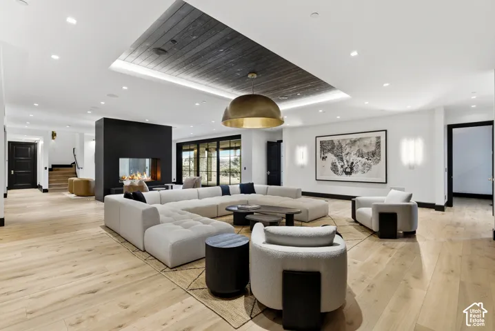 Spacious open-concept living area featuring light wood-finish flooring throughout, a curved sectional seating arrangement, and a coffered ceiling with integrated recessed lighting