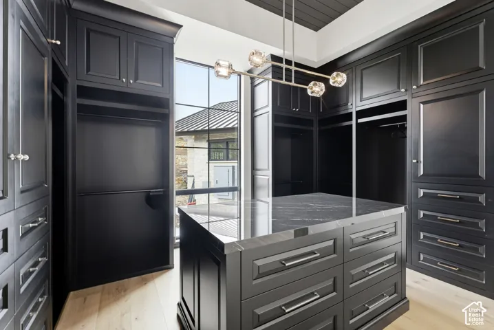 Custom built-in cabinetry with panel detailing, central island with a stone countertop, engineered wood-finish flooring, and contemporary pendant lighting