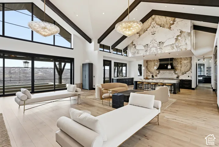Vaulted ceilings with exposed beams, wood-finish flooring, two crystal chandeliers, a kitchen island with built-in seating, and a large sliding glass door