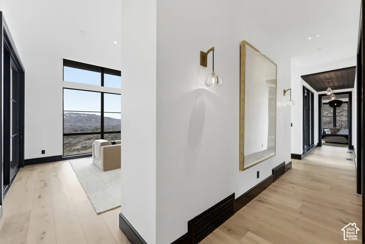 Light wood-finish flooring, dark trim, wall sconces, recessed lighting, and expansive windows
