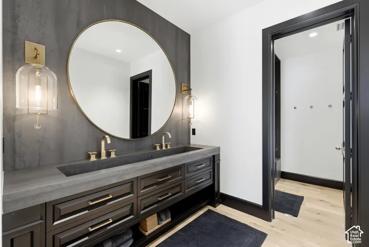 Dual basin vanity with an integrated sink and brass fixtures, dark wood cabinetry, large circular mirror, and wall-mounted sconces