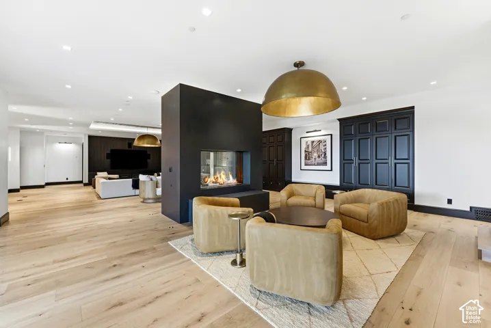 Spacious interior featuring wide-plank wood-finish flooring, a modern linear fireplace, recessed lighting, and a large brass pendant fixture