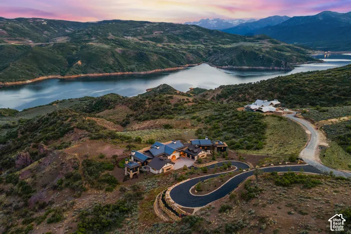 Expansive property featuring a curving paved driveway, multiple structures, and surrounding natural landscape with a large body of water and mountains