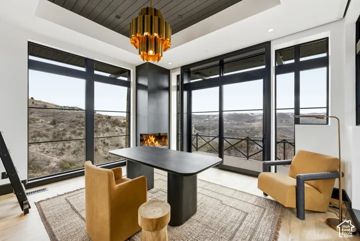 Full-height windows with dark trim, a built-in fireplace, a dark wood-finish ceiling, light wood-finish flooring, and a contemporary chandelier