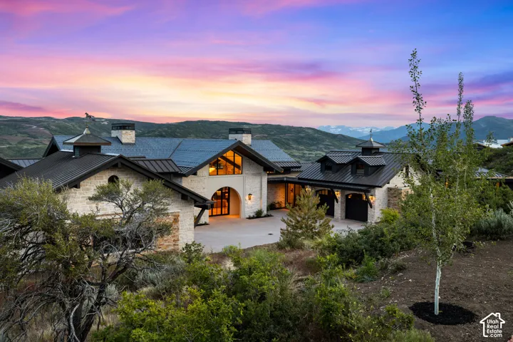 Stone facade residence featuring a prominent arched entry, multiple gabled roofs with dark metal, and integrated garages with carriage-style doors