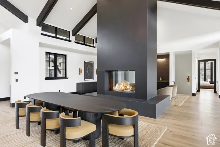 Vaulted ceiling with exposed beams, light wood-finish flooring, built-in fireplace, black framed windows, and recessed lighting