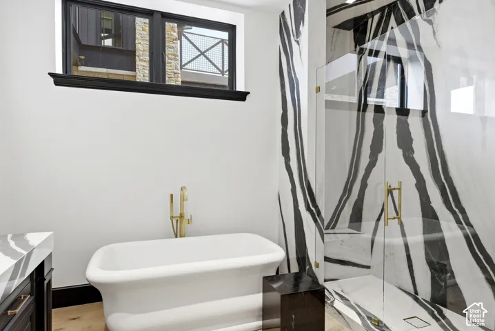 Freestanding soaking tub with a gold-finish faucet, black and white veined stone shower enclosure with a glass door, and a dark wood vanity with a white veined stone countertop