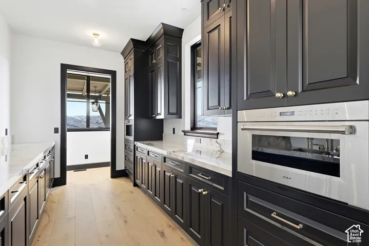 Built-in stainless steel oven, dark custom cabinetry, marble countertops, wood-finish flooring, and a large window with mountain scenery