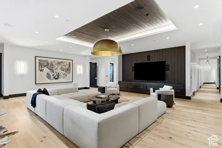 Spacious living area featuring light wood-finish flooring, a wood-paneled accent ceiling with recessed lighting, and a dark wood entertainment wall with built-in cabinetry