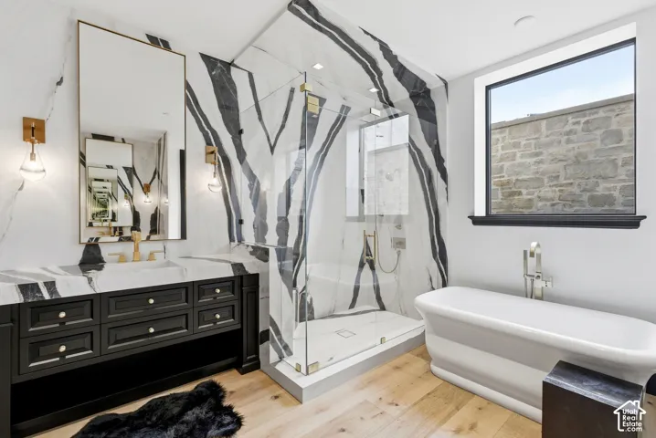 Modern bathroom featuring a freestanding tub, glass-enclosed shower, large vanity with ample storage, contemporary wall sconces, and wood-finish flooring