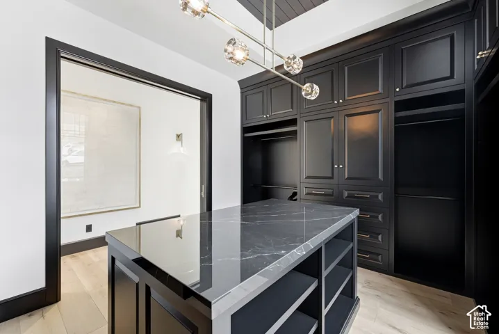Custom built-in cabinetry, dark stone-finish island with integrated shelving, decorative overhead lighting fixture, light wood-finish flooring, and dark trim details