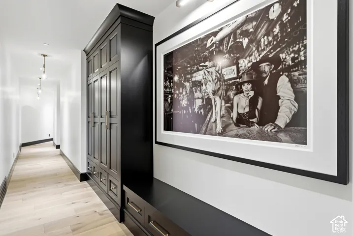 Long hallway featuring light-toned wood-finish flooring, dark built-in cabinetry with paneled doors, and contemporary pendant lighting fixtures