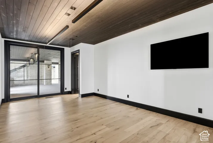Wood-finish flooring with black baseboards, white walls, and a dark wood-paneled ceiling