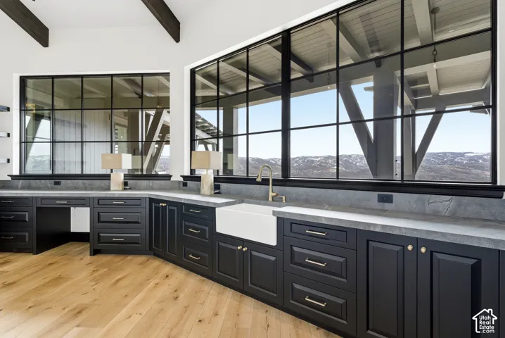 Expansive window wall with black gridded frames, built-in cabinetry with stone countertops, integrated farmhouse sink with a gooseneck faucet, and light wood-finish flooring