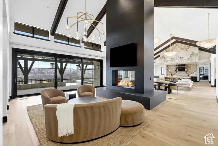 Vaulted ceilings with exposed beams, light wood-finish flooring, a modern linear fireplace, and expansive glass sliding doors