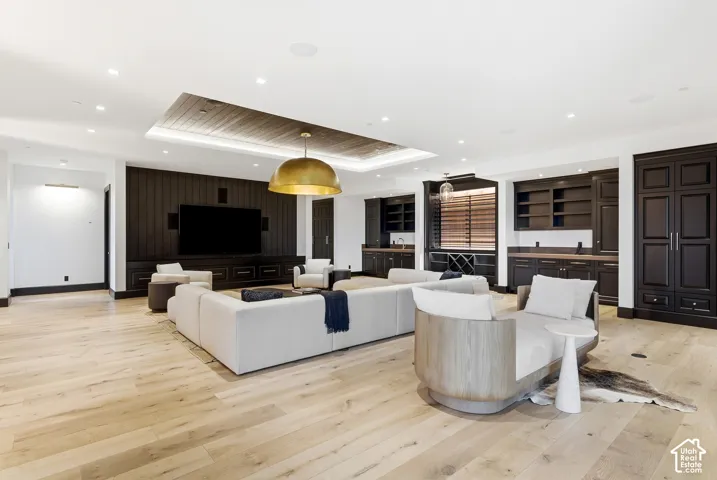 Spacious entertainment area with light wood-finish flooring, a dark wood paneled media wall, and a coffered ceiling with recessed lighting