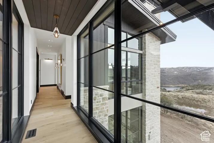 Expansive window walls, wood-finish flooring, stone exterior accents, dark wood-paneled ceiling, and recessed lighting