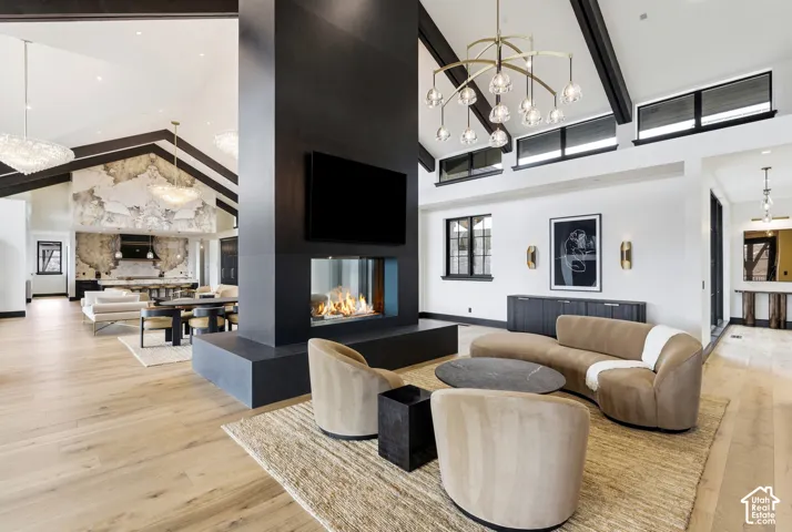 Vaulted ceiling with exposed beams, wood-finish flooring, two-sided fireplace, modern chandelier, and transom windows