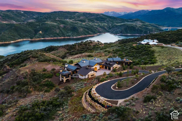 Expansive property featuring a winding paved driveway, multi-level dwelling with multiple rooflines, and a serene lake backdrop