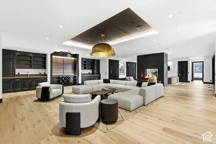 Hardwood flooring throughout, built-in wet bar with wood countertop, contemporary fireplace feature, recessed lighting, and a detailed wood ceiling panel with central pendant light