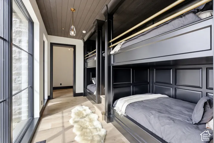 Built-in bunk beds with paneled detailing, wood-finish flooring, dark wood-paneled ceiling, black framed windows, and a hanging pendant light fixture