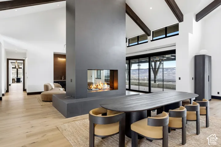 Vaulted ceilings with exposed beams, modern central fireplace, expansive glass doors, wood-finish flooring, and a built-in wet bar with dark tile