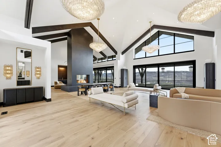 Vaulted ceiling with exposed wood beams, wood-finish flooring, built-in fireplace, large-format windows, and multiple chandeliers