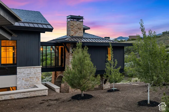 Exterior featuring black siding, stone accents, a glass-enclosed walkway, and a prominent stone chimney