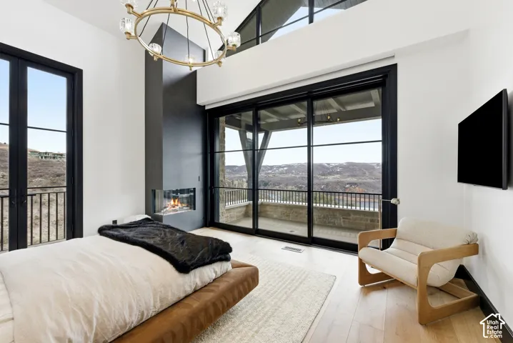 Hardwood flooring, black-framed sliding glass doors, built-in fireplace with a glass front, black-framed French doors, and a gold-tone chandelier
