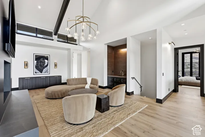Vaulted ceiling with exposed beams, wood-finish flooring, built-in wet bar, and a contemporary chandelier