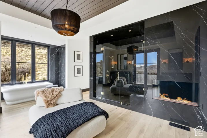 Freestanding soaking tub, wood-finish flooring, built-in fireplace, glass-enclosed shower, and dark-toned accent walls