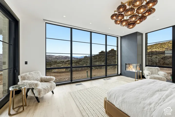 Expansive floor-to-ceiling windows, wood-finish flooring, a modern built-in fireplace with a dark surround, and a distinctive multi-light chandelier