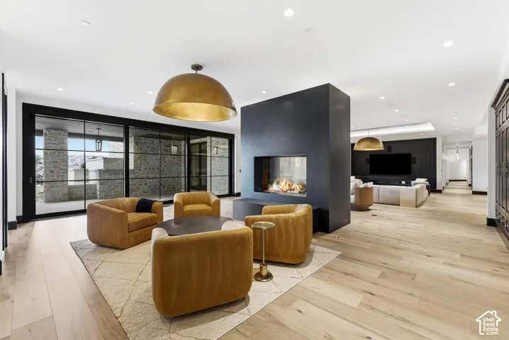 Expansive open-concept living area featuring light wood-finish flooring, a contemporary fireplace, and a large gold-finish pendant light fixture