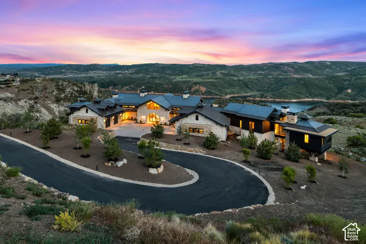 Expansive property featuring a stone and dark-clad exterior, multi-tiered roofline, a curved paved driveway, and established landscaping