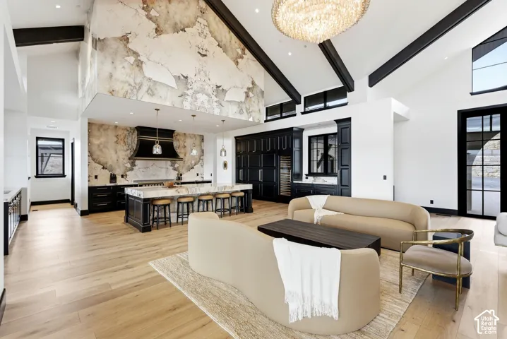 Vaulted ceiling with exposed beams, light wood-finish flooring, full-height decorative stone wall, large kitchen island with seating, and a built-in beverage refrigerator