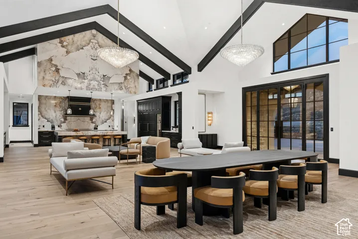 Open-concept living area with vaulted ceilings and exposed beams, wood-finish flooring, a kitchen featuring a stone slab accent wall and island, and a wall of multi-pane glass doors